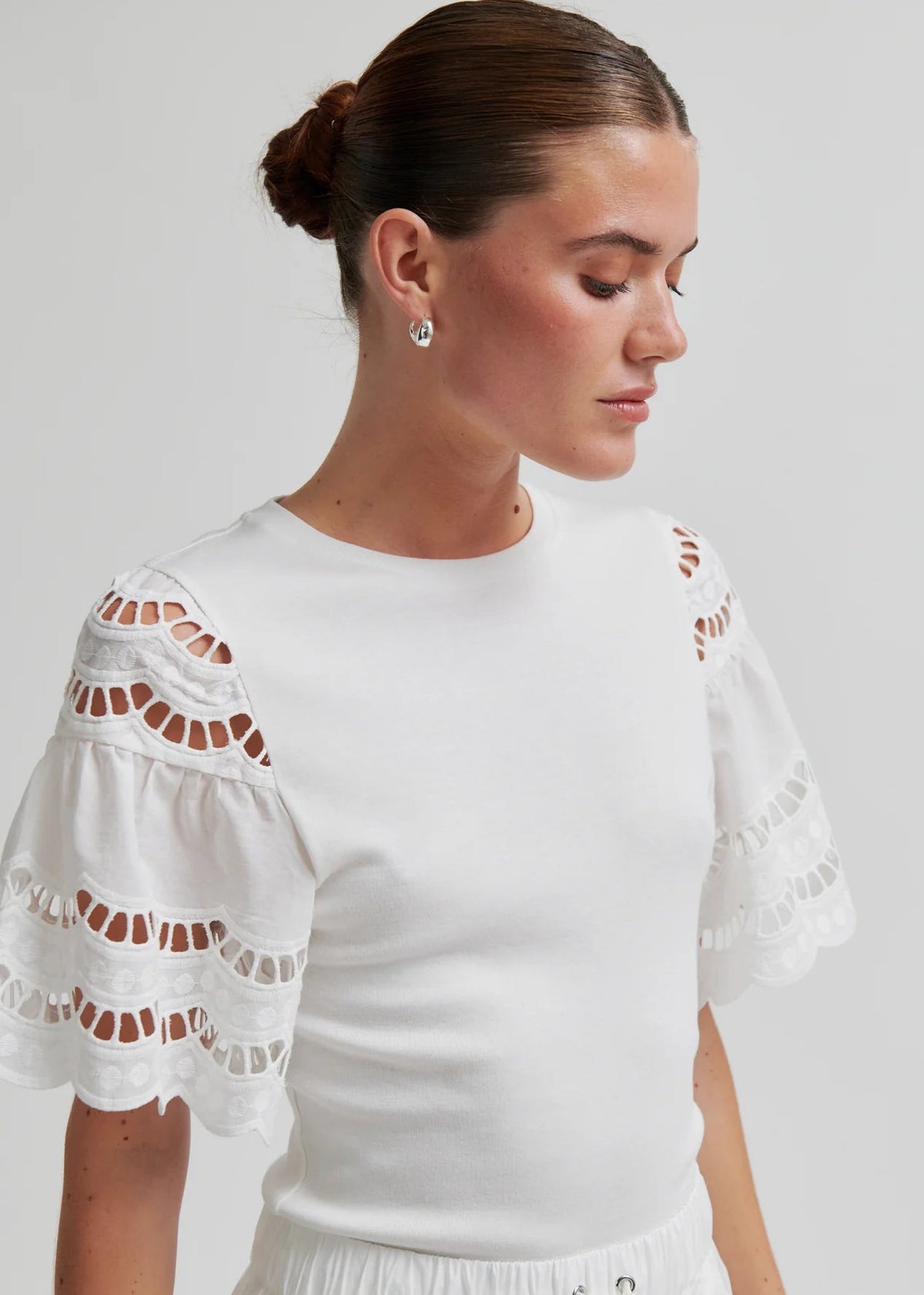 Woman wearing a white outfit with decorative sleeves on a plain background