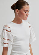 Woman wearing a white outfit with decorative sleeves on a plain background