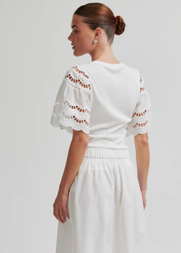 Woman wearing a white outfit with decorative sleeves on a plain background