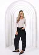 Woman in a beige top and black pants standing in a white geometric archway.
