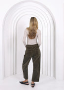 Woman wearing a beige top and green pants standing in front of a white archway.