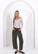 Woman wearing a beige top and green pants standing in front of a white archway.