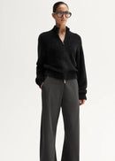 Woman wearing a black sweater and grey pants on a white background
