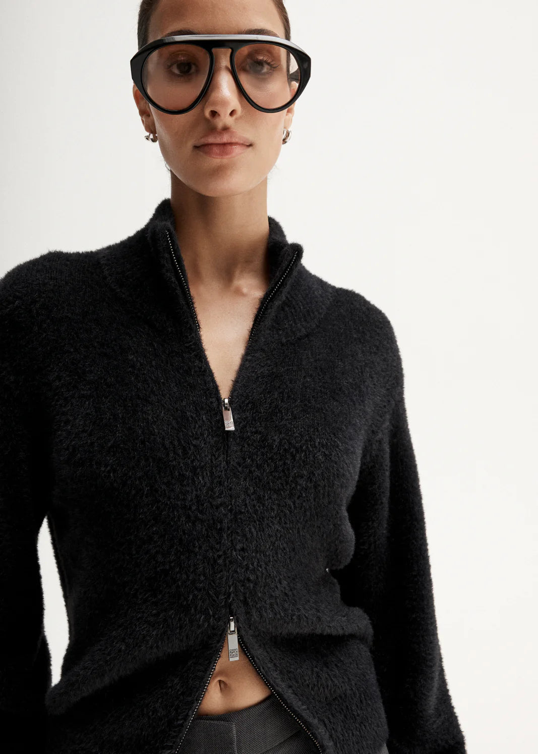 Woman wearing a black sweater and grey pants on a white background