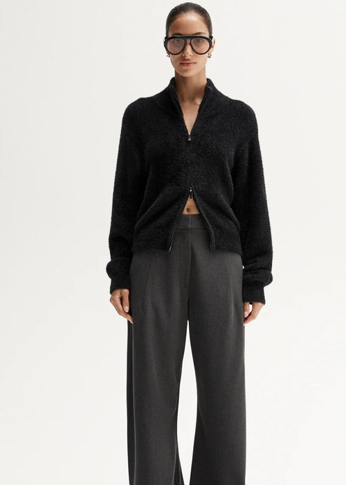 Woman wearing a black sweater and grey pants on a white background