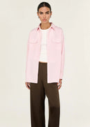 Person wearing a pink shirt over a white top with brown pants on a white background