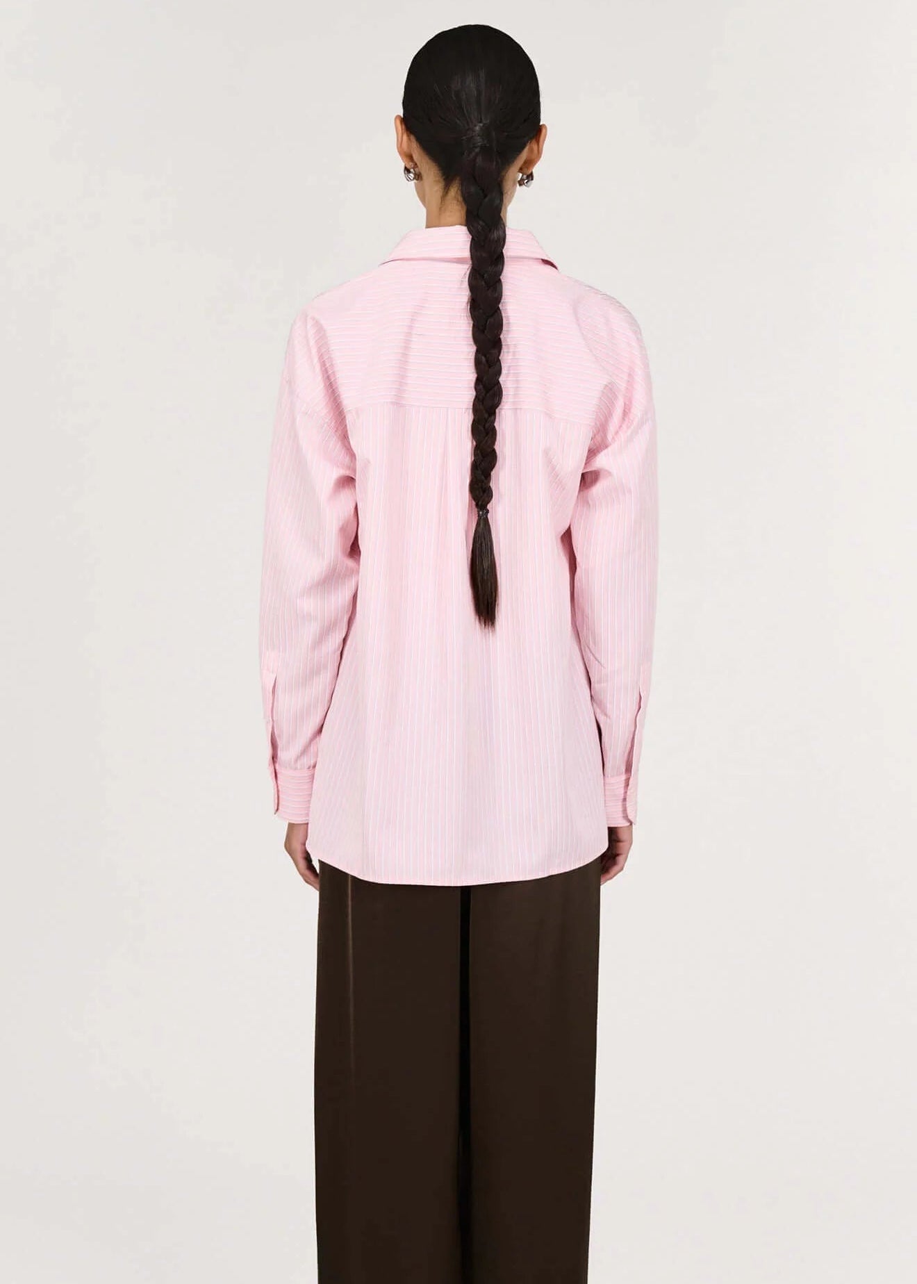 Person wearing a pink shirt and brown pants on a white background