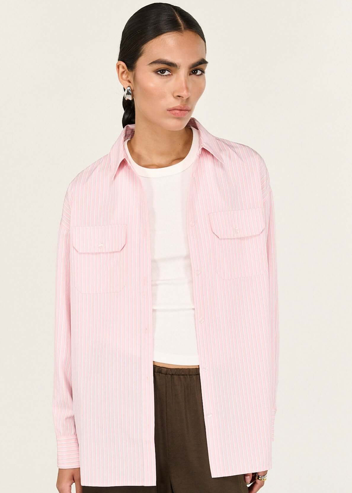 Person wearing a pink shirt over a white top with brown pants on a white background