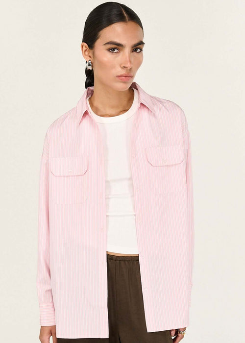 Person wearing a pink shirt over a white top with brown pants on a white background