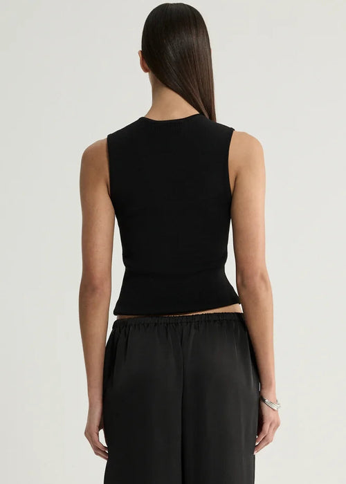 A woman shown from the back wearing a black sleeveless ribbed crop top and black wide-leg trousers against a plain light gray studio background.