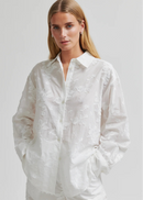 Woman wearing a white button-up shirt and pants on a plain background