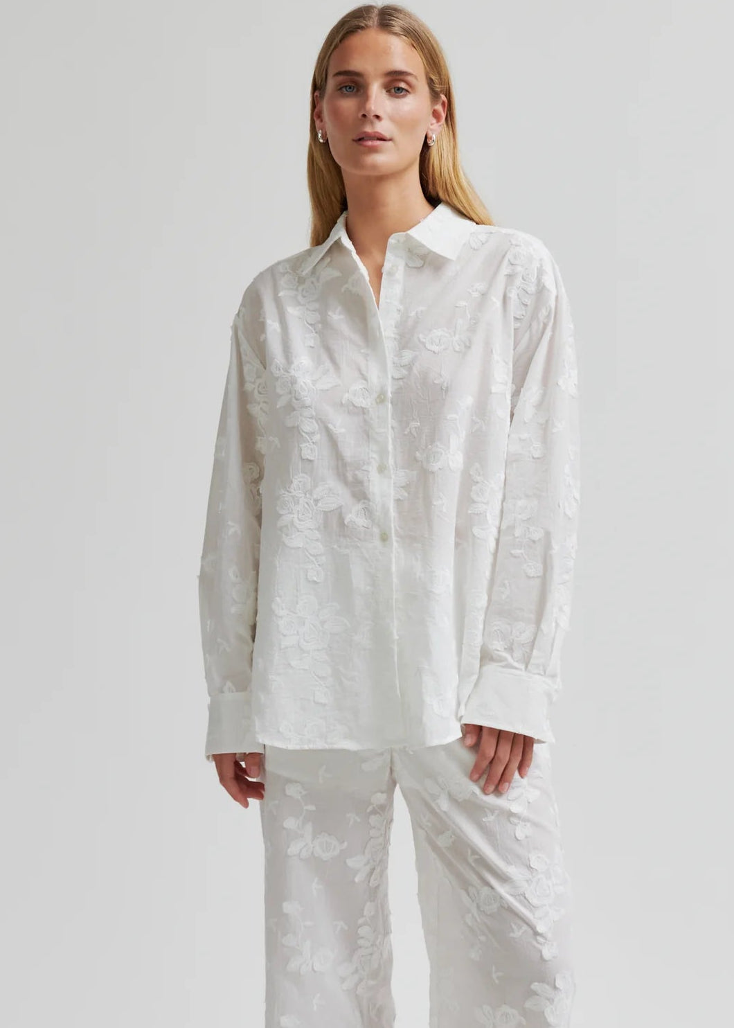 Woman wearing a white button-up shirt and pants on a plain background