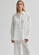 Woman wearing a white button-up shirt and pants on a plain background