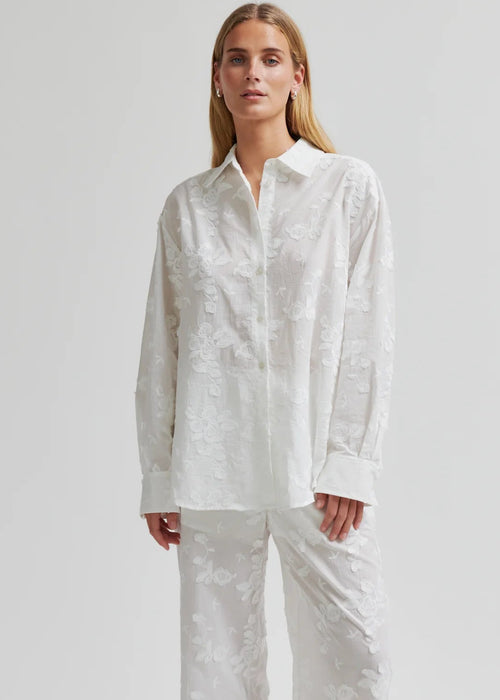 Woman wearing a white button-up shirt and pants on a plain background