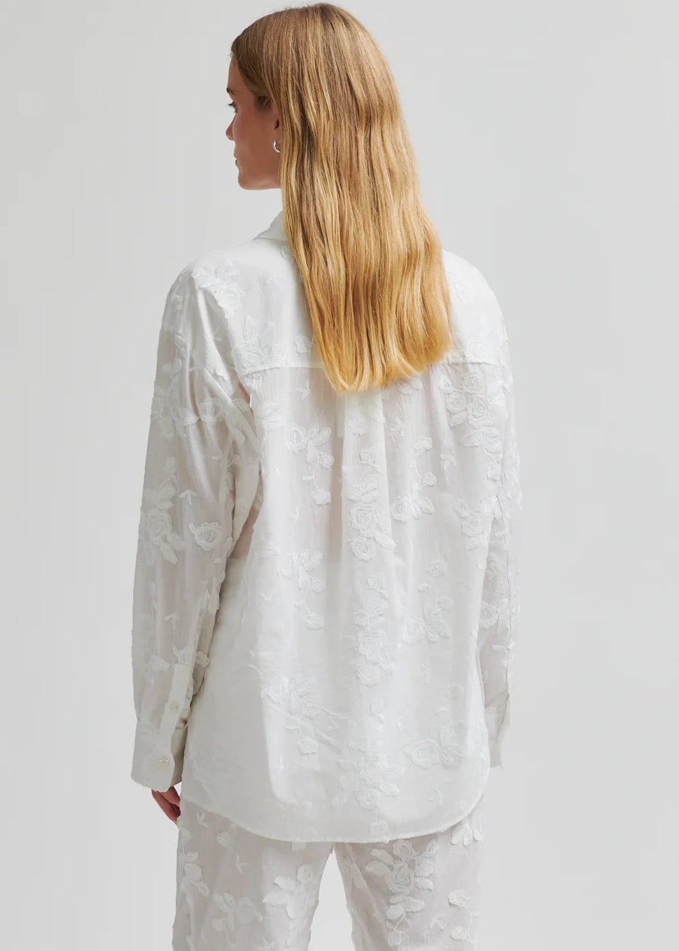 Woman wearing a white button-up shirt and pants on a plain background
