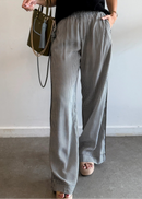 Woman wearing a black sleeveless top and checkered pants, holding a green handbag indoors.