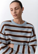 Woman wearing a striped sweater with brown and blue horizontal stripes on a light background
