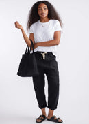 Woman holding a black woven bag wearing a white t-shirt and black pants on a white background