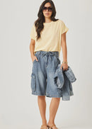 Woman wearing a yellow top and denim cargo shorts on a white background