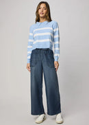 Woman wearing a blue and white striped sweater and wide-leg jeans on a gray background