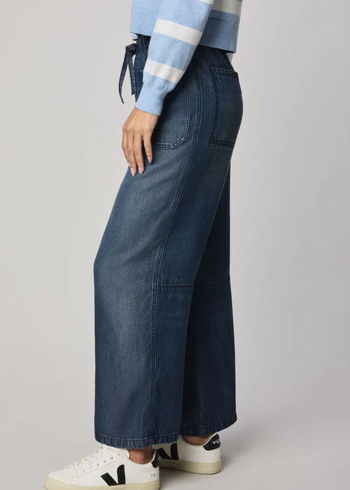 Woman wearing a blue and white striped sweater and wide-leg jeans on a grey background