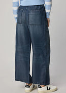 Woman wearing a blue and white striped sweater and wide-leg jeans on a grey background