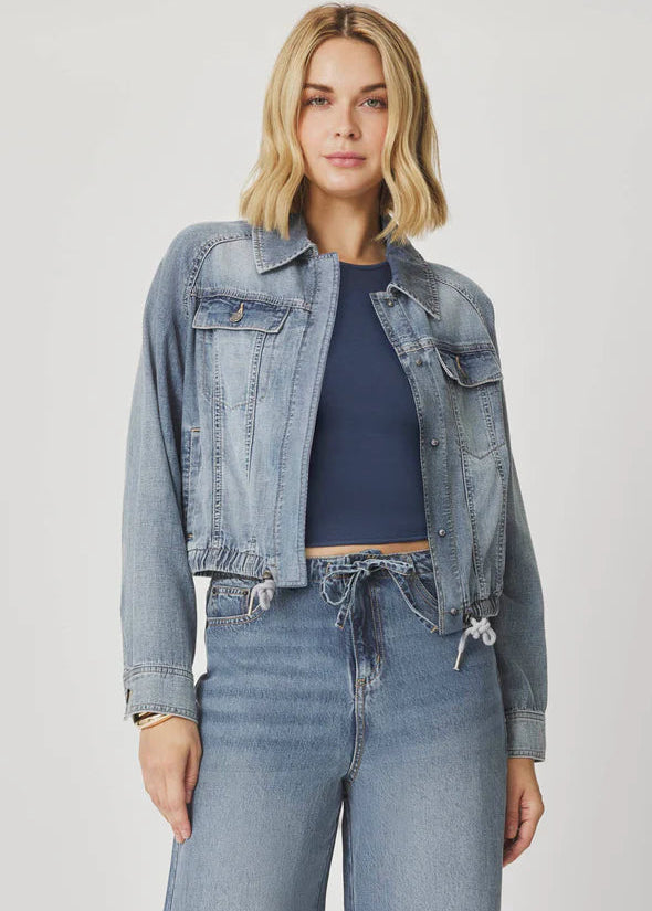 Woman wearing a denim jacket and jeans on a plain background