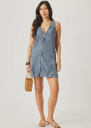 Woman wearing a denim dress holding a woven bag on a plain background