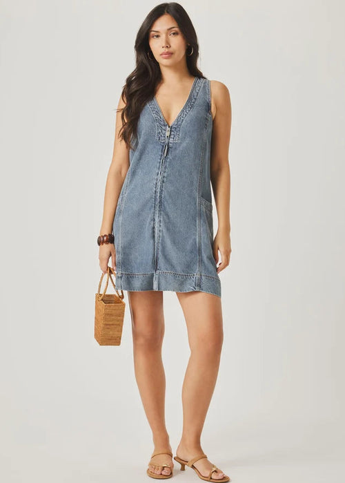 Woman wearing a denim dress holding a woven bag on a plain background