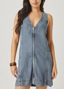 Woman wearing a denim dress holding a woven bag on a plain background