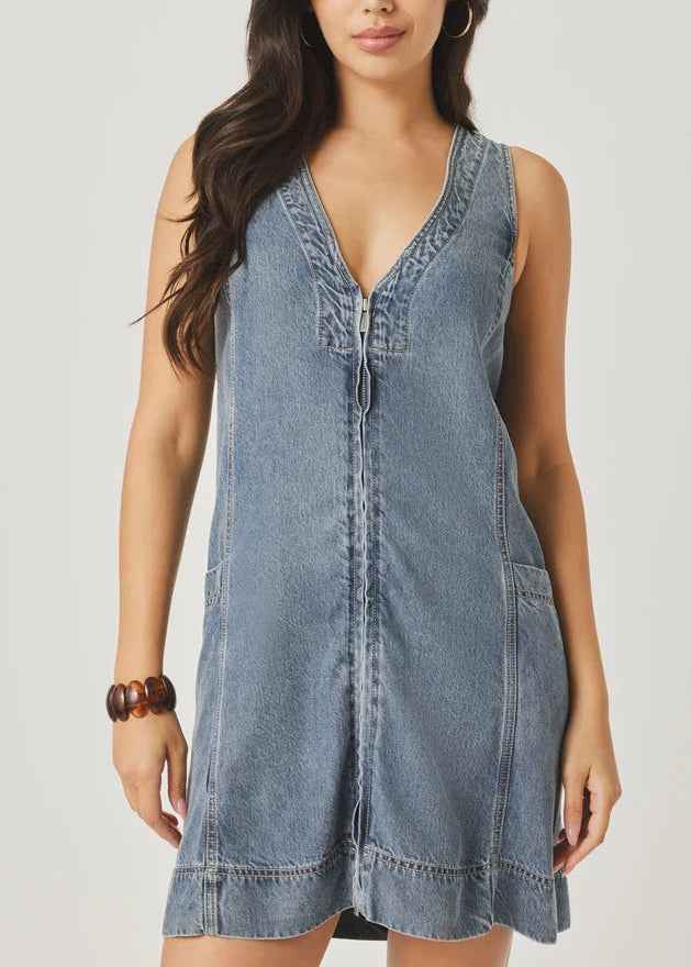 Woman wearing a denim dress holding a woven bag on a plain background