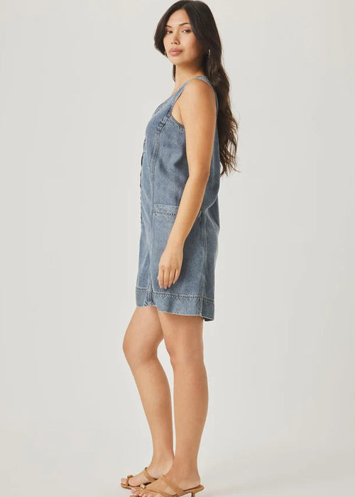Woman wearing a denim dress holding a woven bag on a plain background