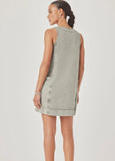 A woman modelling a sleeveless, V-neck mini dress with a faded green wash and decorative trim, paired with pink sandals, against a light grey studio background.