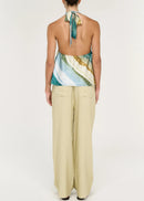 Women wearing halter neck green top with beige pants on white background viewed from the back