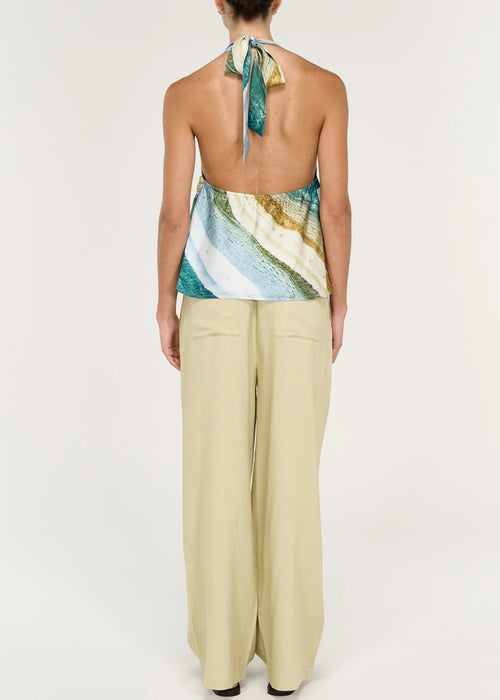 Women wearing halter neck green top with beige pants on white background viewed from the back