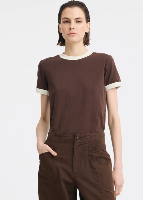 A model wearing a brown short-sleeve t-shirt with cream ribbed trim at the crew neck and sleeve cuffs, paired with brown wide-leg trousers, against a light grey studio background.