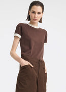A model wearing a brown short-sleeve t-shirt with cream ribbed trim at the crew neck and sleeve cuffs, paired with brown wide-leg trousers, against a light grey studio background.
