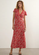 A woman modelling a red midi-length dress with a white floral pattern, short flutter sleeves, and a V-neckline, standing against a plain off-white studio wall.