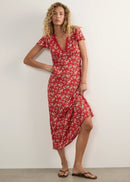 A woman modelling a red midi-length dress with a white floral pattern, short flutter sleeves, and a V-neckline, standing against a plain off-white studio wall.