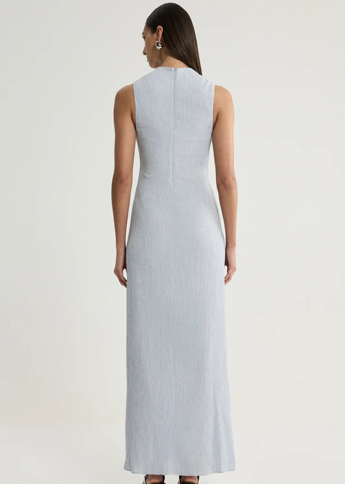 A woman viewed from the back wearing a sleeveless, floor-length light blue dress against a plain light grey studio background.