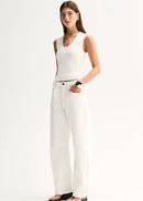 A woman modelling a white sleeveless top and white wide-leg trousers against a plain white studio background.