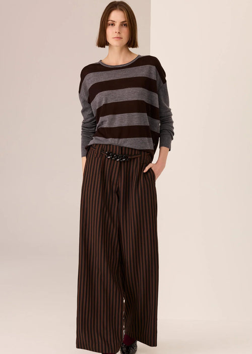 Woman wearing a striped sweater and wide-leg pants on a plain background