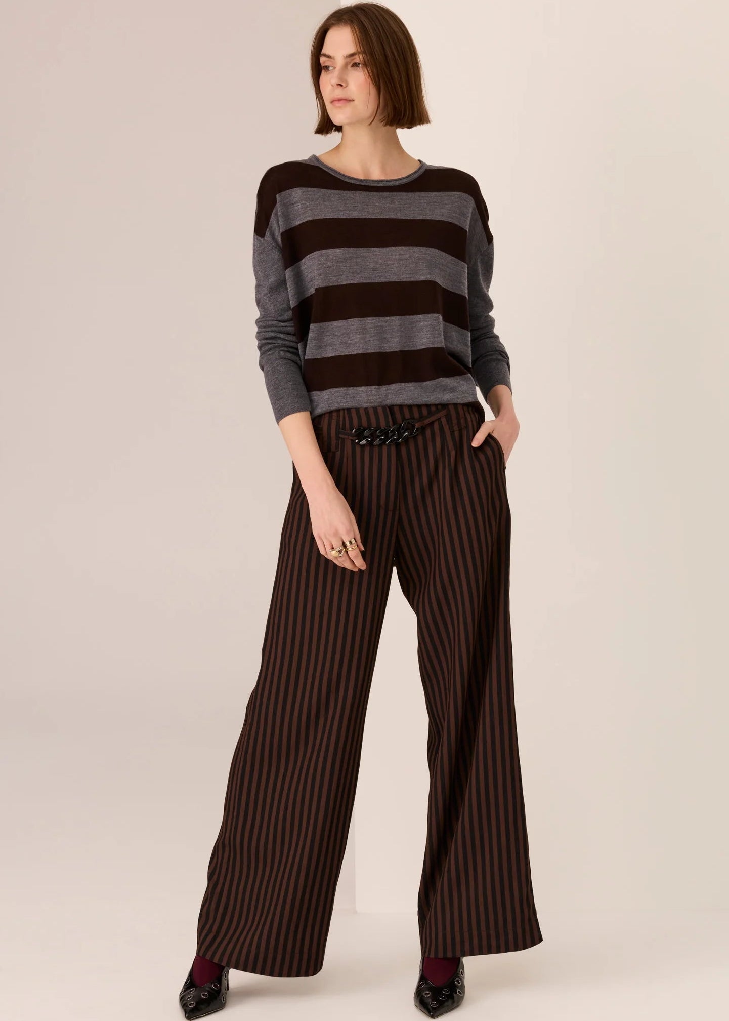 Woman wearing a striped sweater and wide-leg pants on a plain background