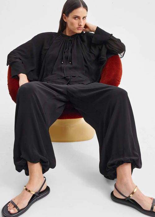 Woman sitting on a red chair wearing a black outfit with a white background
