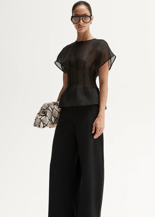 Woman wearing a black outfit with a sheer top and wide-leg pants, holding a patterned clutch.