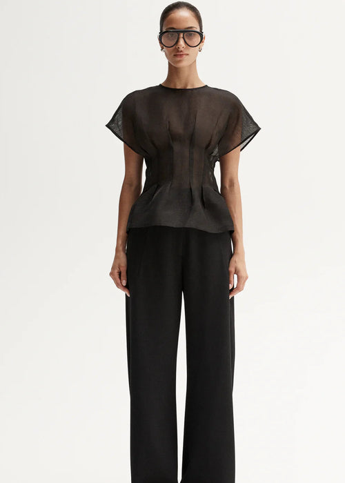Woman wearing a black outfit with a sheer top and wide-leg pants, holding a patterned clutch.