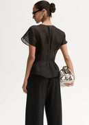 Woman wearing a black outfit with a sheer top and wide-leg pants, holding a patterned clutch.