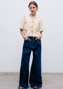 Woman wearing a beige embroidered top and blue wide-leg pants against a white background