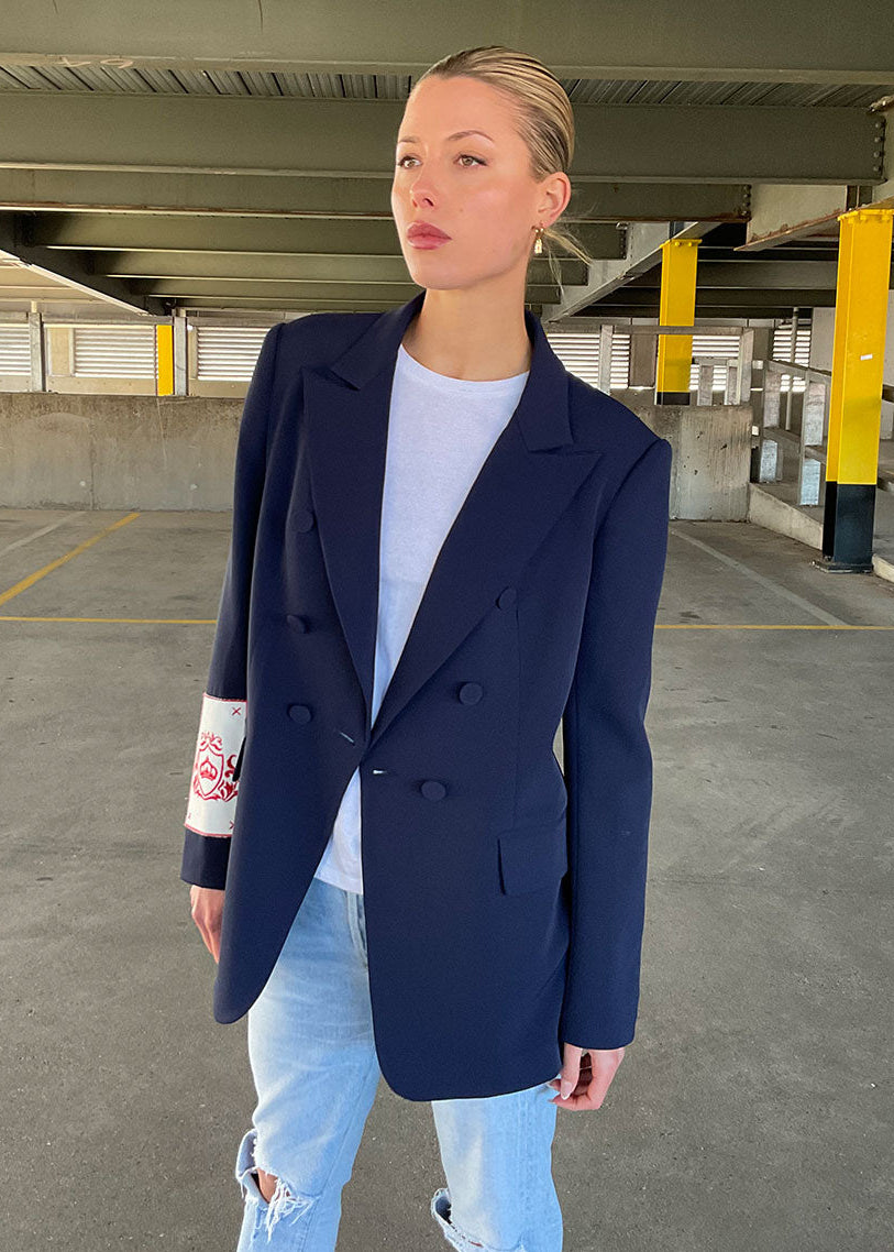 Woman wearing a navy blazer over a light blue shirt and jeans in an underpass.