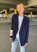Woman wearing a navy blazer over a light blue shirt and jeans in an underpass.